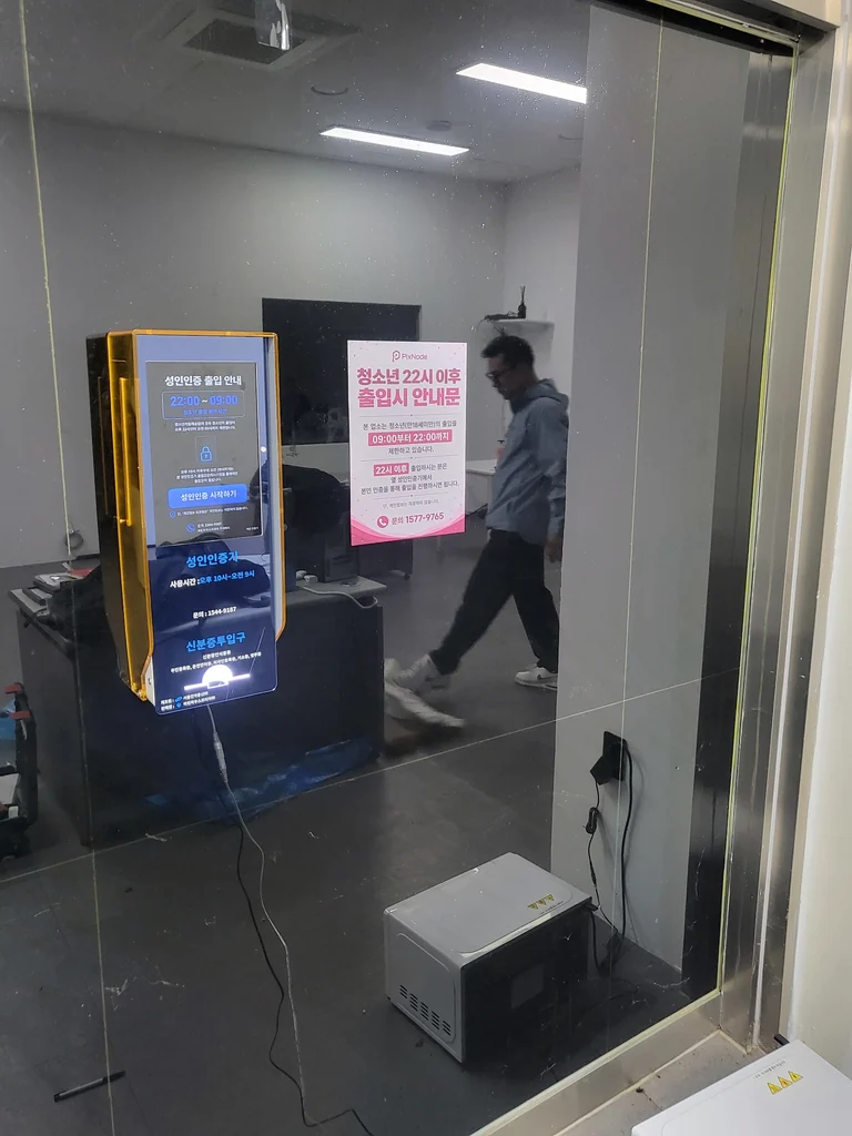 비스듬히 촬영한 유리 출입구와 성인인증기 설치 전경