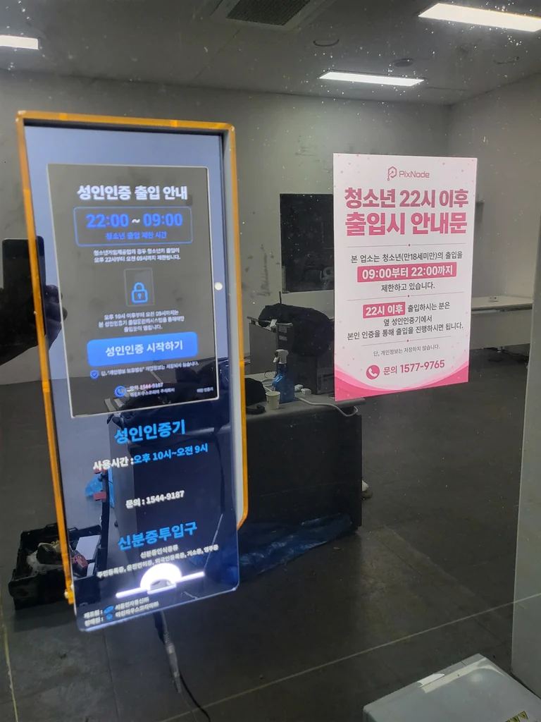 유리 출입구에 설치된 성인인증기와 옆에 부착된 출입 안내문